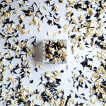 A small square glass container filled with dried flower petals, placed on a white surface and scattered petals
